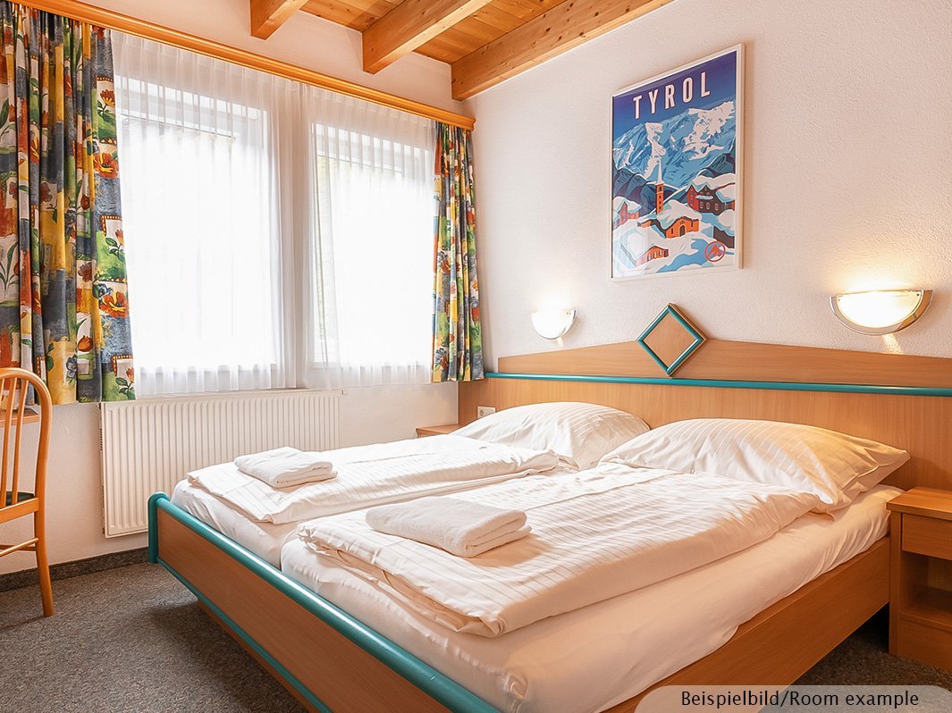 Das Bild zeigt ein Doppelbett mit zwei direkt anschließenden Nachtschränken, zwei Lampen links und rechts vom Bett, Bild, Heizung, Büro mit Stuhl, Fenster