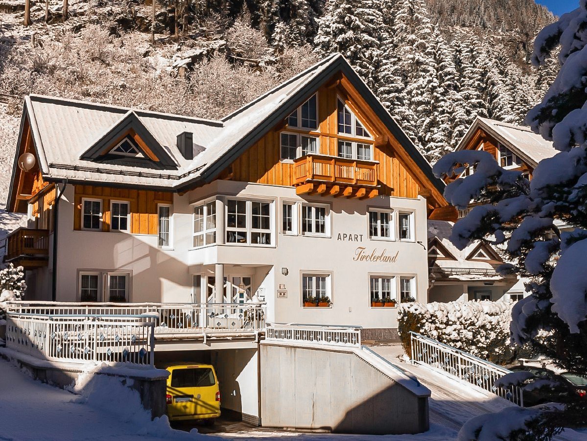 Das Bild zeigt zeigt das Apart Tiroler Land von außen mit Auffahrt und Garage, Autos, Veranda