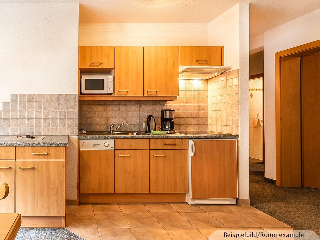 Das Bild zeigt Küchenzeile inklusive Wasserkocher, Kaffeemaschine, Spülmaschine, Mikrowelle, links davon separate Arbeitsplatte, Kühlschrank, Herd, Dunstabzugshaube, Küchenschränke, Waschbecken   
