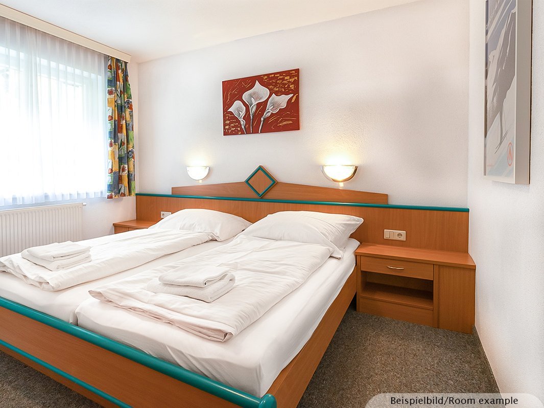 Das Bild zeigt ein Doppelbett mit zwei direkt anschließenden Nachtschränken, zwei Lampen links und rechts vom Bett, Bild, Heizung, Fenster  
