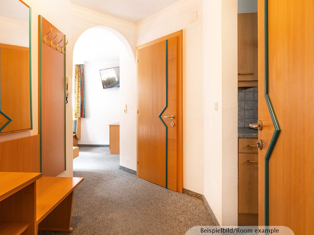 Das Bild zeigt Flur mit Spiegel, Garderobe, Kommode, TV, Ansätze der Küchenzeile, Ansätze des Wohnzimmers, Fenster 