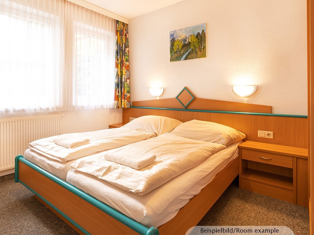 Das Bild zeigt ein Doppelbett mit zwei direkt anschließenden Nachtschränken, zwei Lampen links und rechts vom Bett, Bild, Heizung, Fenster
