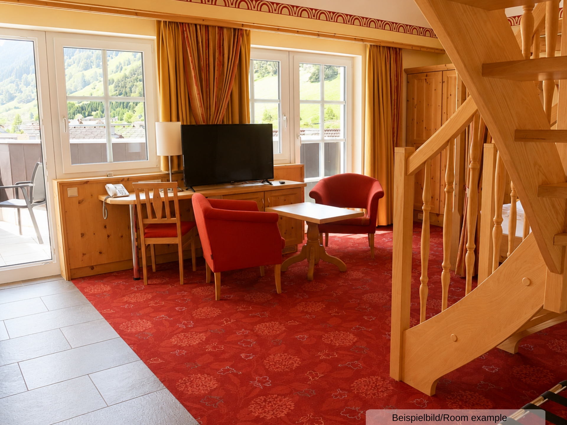 Beispielbild des Wohnbereichs der Juniorsuite, mit Sitzgelegenheit, TV, Treppenaufgang und Zugang zum Balkon