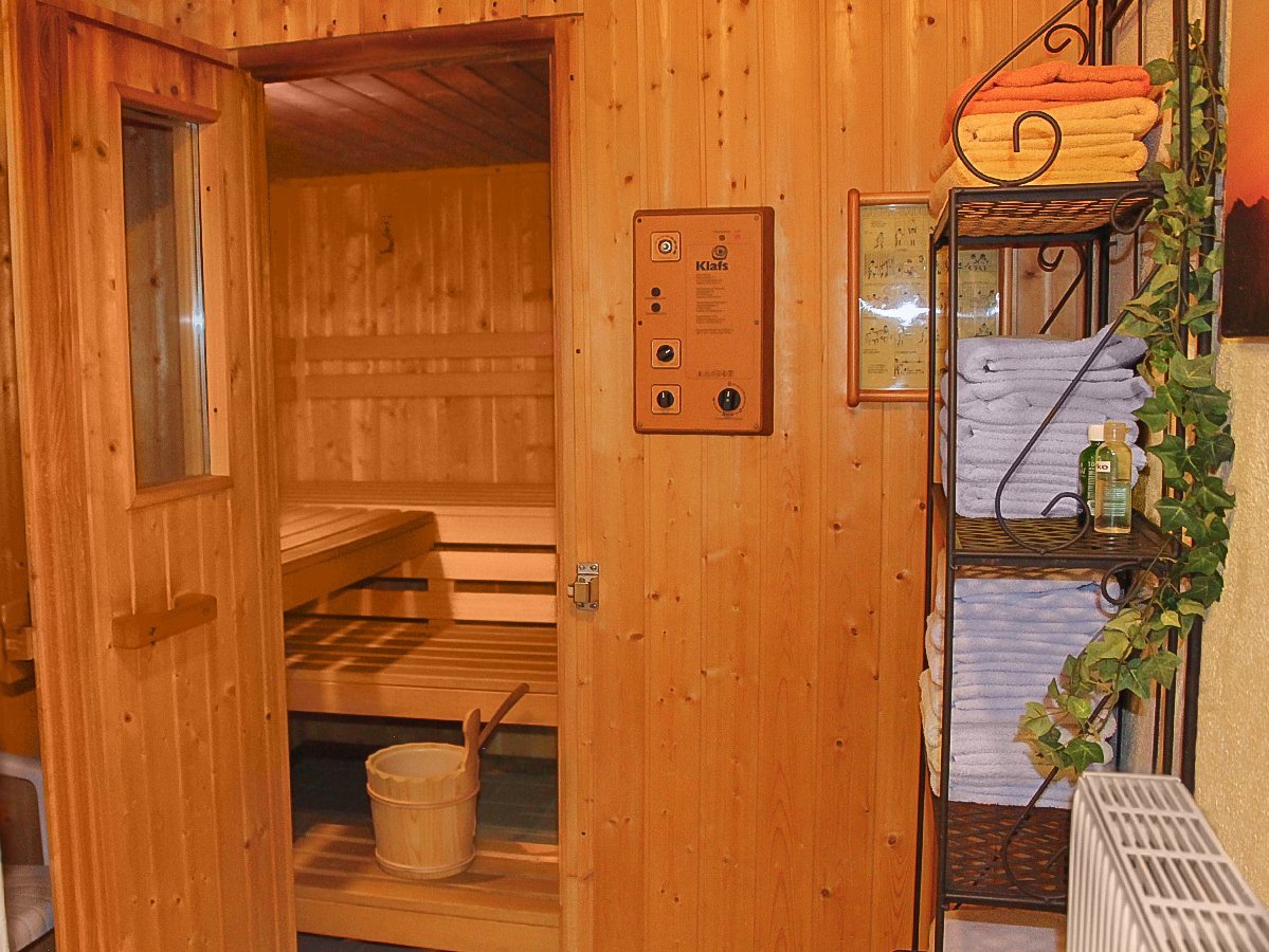 Das Bild zeigt eine Sauna und davor steht ein kleines Regal mit Handtüchern