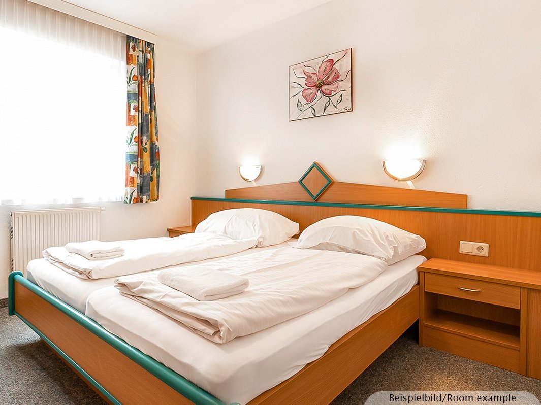 Das Bild zeigt ein Doppelbett mit zwei direkt anschließenden Nachtschränken, zwei Lampen links und rechts vom Bett, Bild, Heizung, Fenster