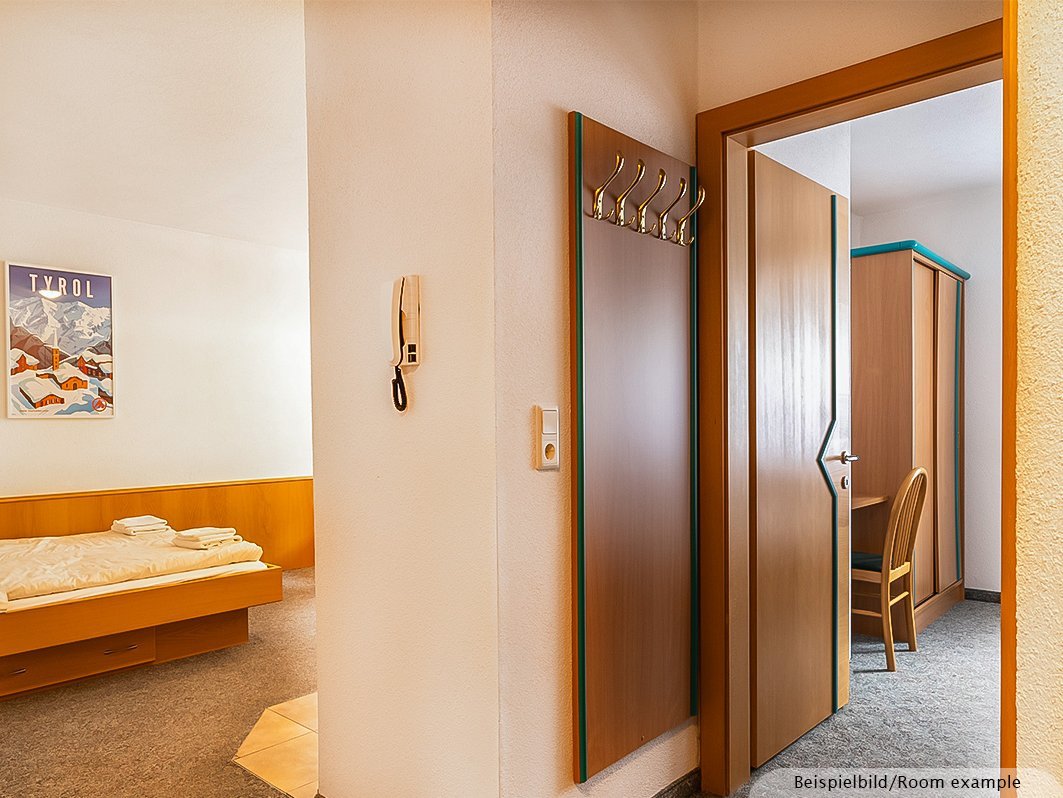 Das Bild zeigt Doppelbett mit Bettwäsche, Bild, Lichtschalter, Telefon, Garderobe, Büro mit Stuhl im Nebenzimmer, Schrank,